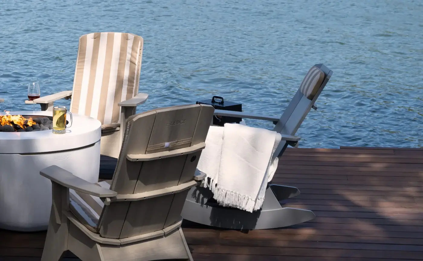 Two Adirondack chairs on a wooden deck by a body of water.