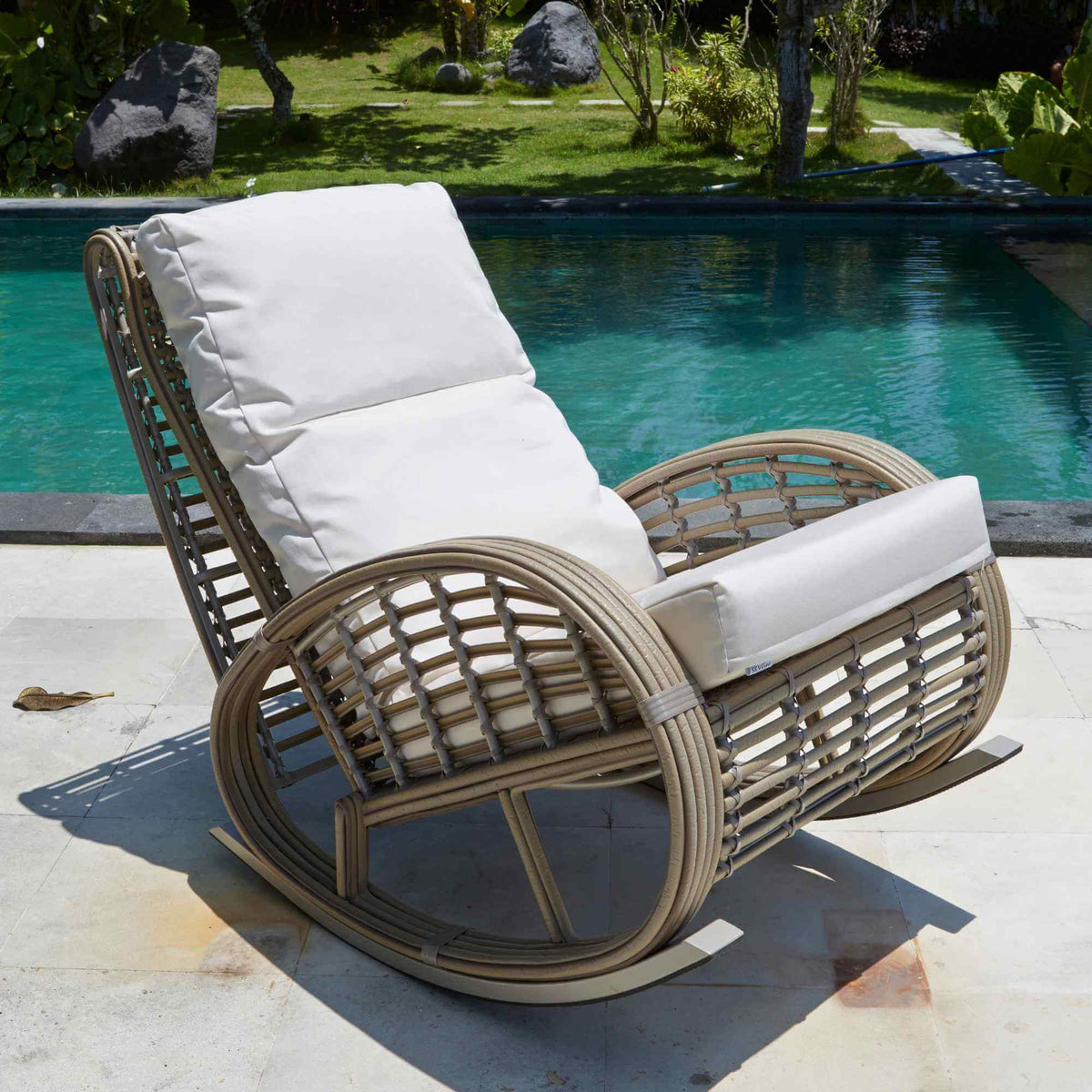 Wicker rocking chair with white cushions by a poolside