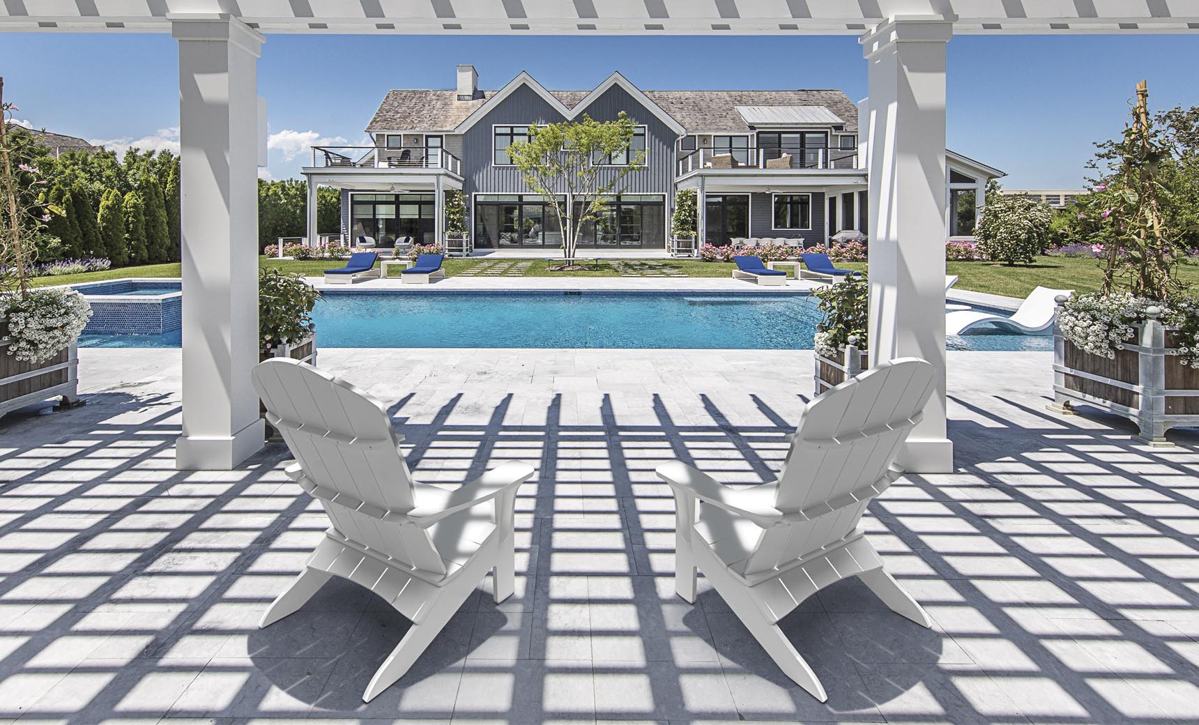 White Legacy Adirondack chairs under a pergola beside a pool