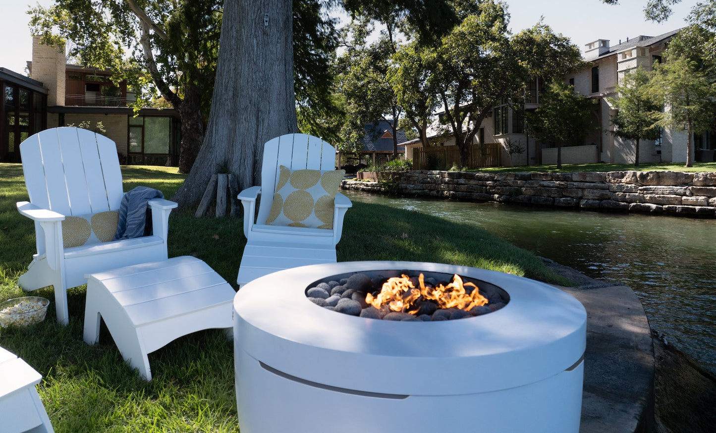 Legacy Adirondack chair paired with its ottoman near a waterway fire pit