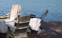 Two Adirondack chairs on a wooden deck by a body of water.