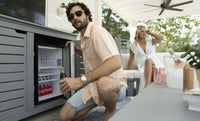 Man opening a refrigerator outdoors with a woman in the background