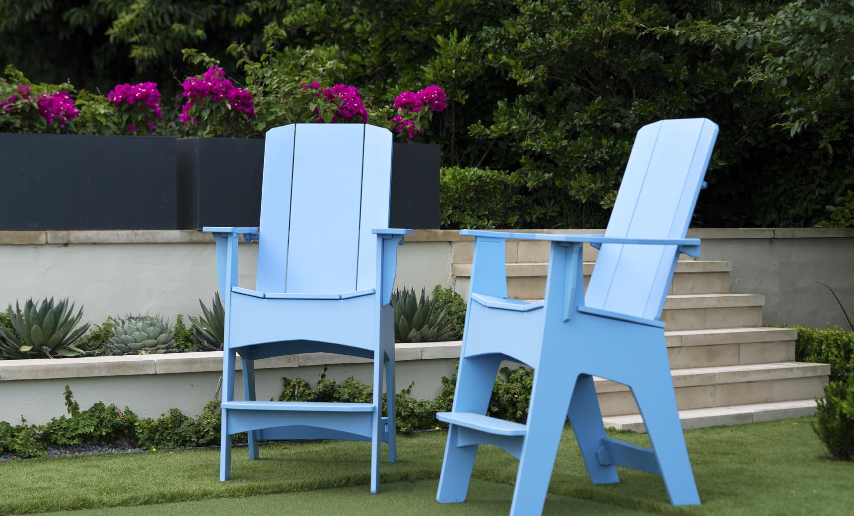 Two tall Mainstay Adirondack chairs in Sky Blue on a lawn with flowers